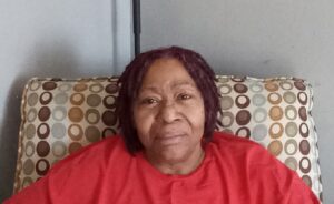 A Black woman with medium brown locs wearing a red shirt smiles at the camera