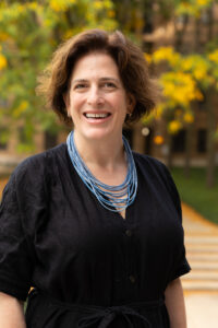 A white woman with brown hair, a black shirt and a blue bead necklace